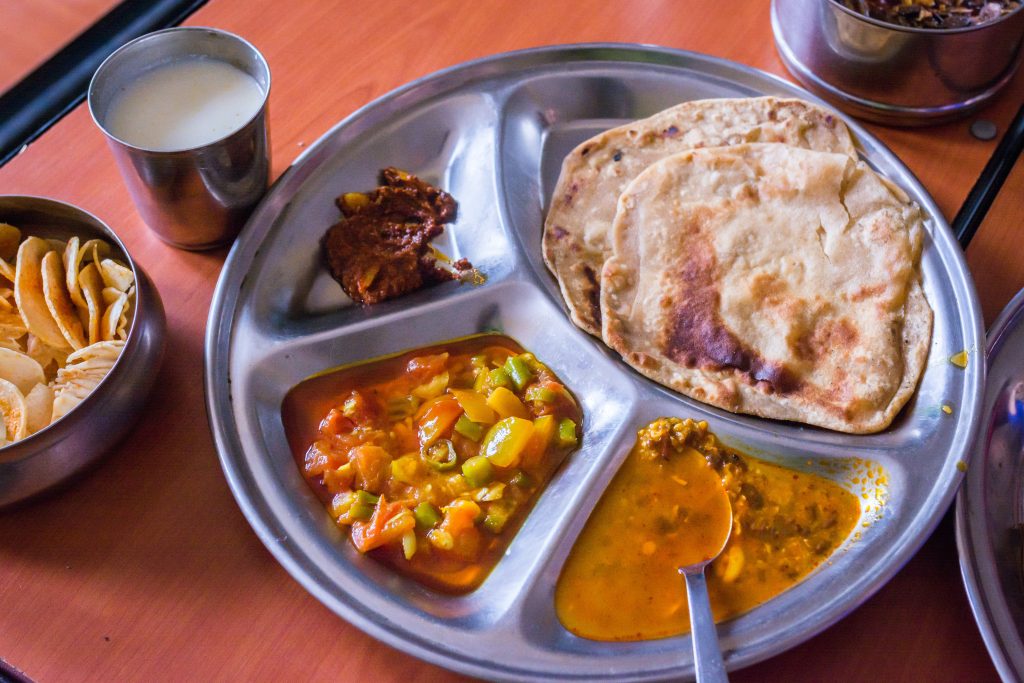 a plate with dal, curry, roti. some butter milk and other healthy food served hot as a nourishing meal