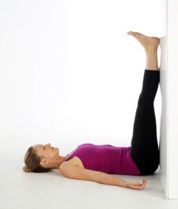 Yoga During Menstruation Cycle, Do's and Don’ts. a woman doing viparita karni or taking legs up against a wall to relieve pain.