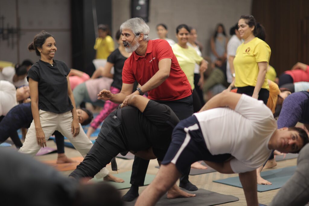 bharat shetty in a workshop correcting a students yoga pose while others are holding revolved side angle pose.