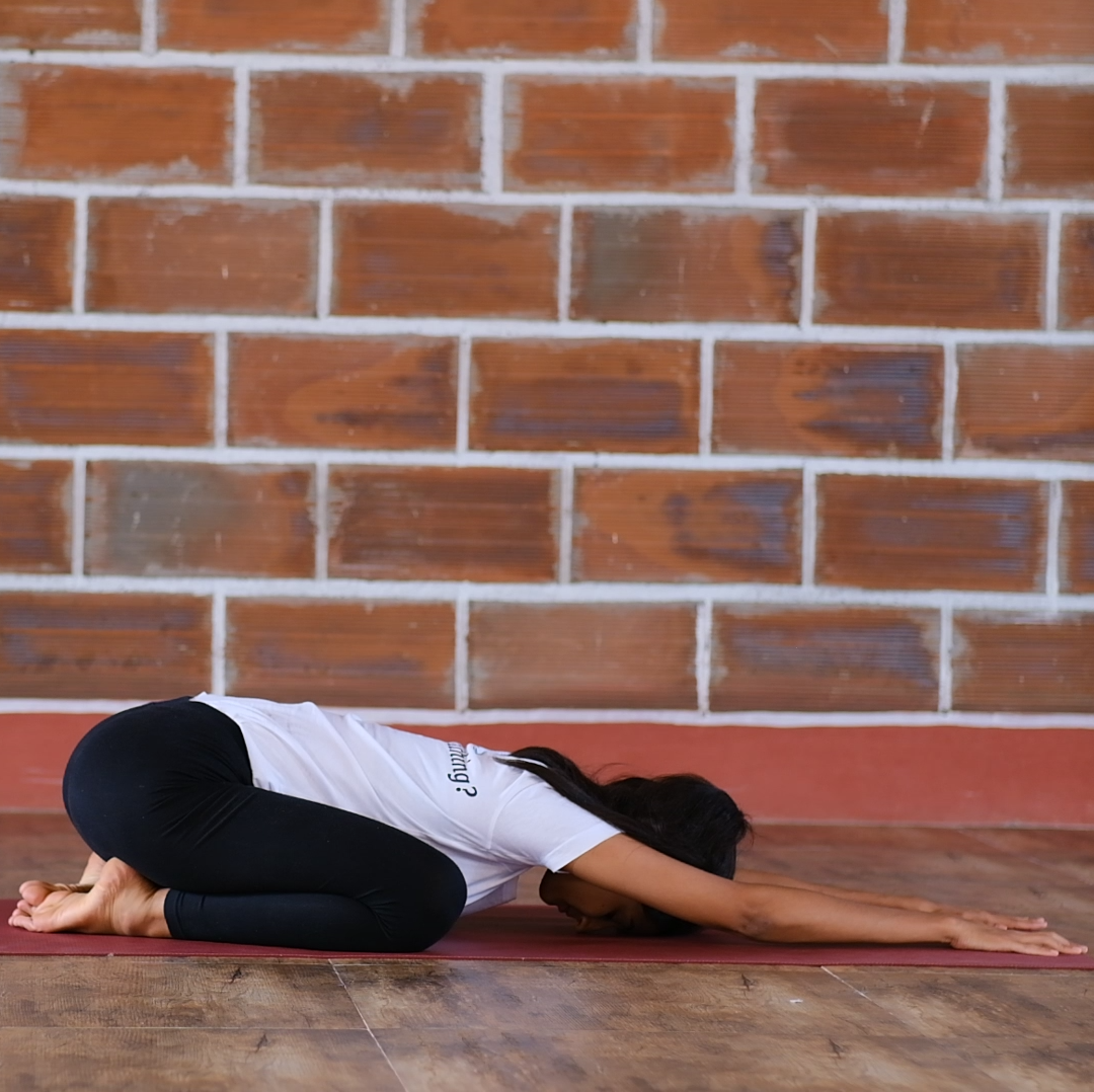 the relaxing sasankasna pose performed by a yoga student in white tshirt.